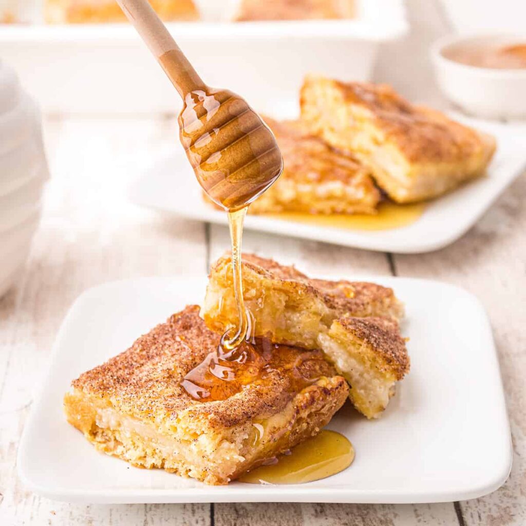 A serving of cream cheese filled crescent roll pastries being drizzled with honey.