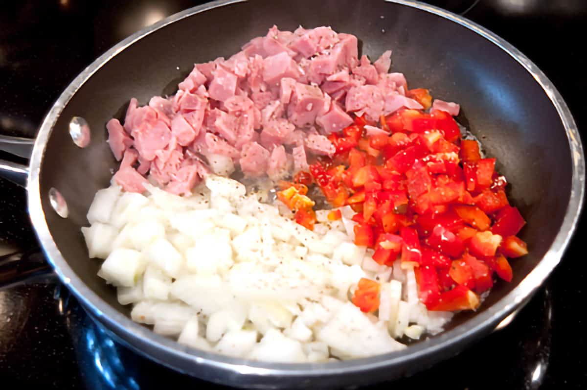 Diced ham, red bell pepper, and onion cooking in a small skillet.