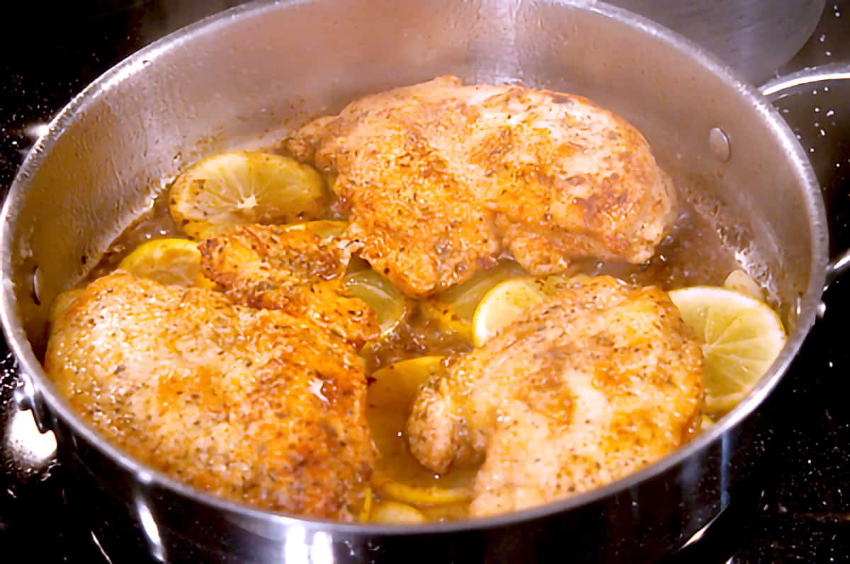 Pan fried chicken and lemon slices in a skillet.