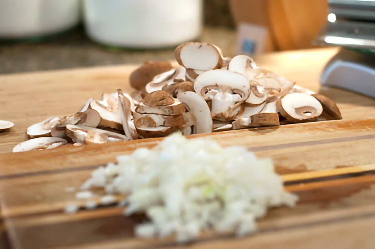 Sliced mushrooms and chopped onions on a cutting board.