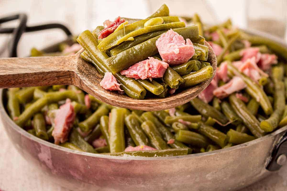 Finished green beans with ham hock on a wooden spoon.