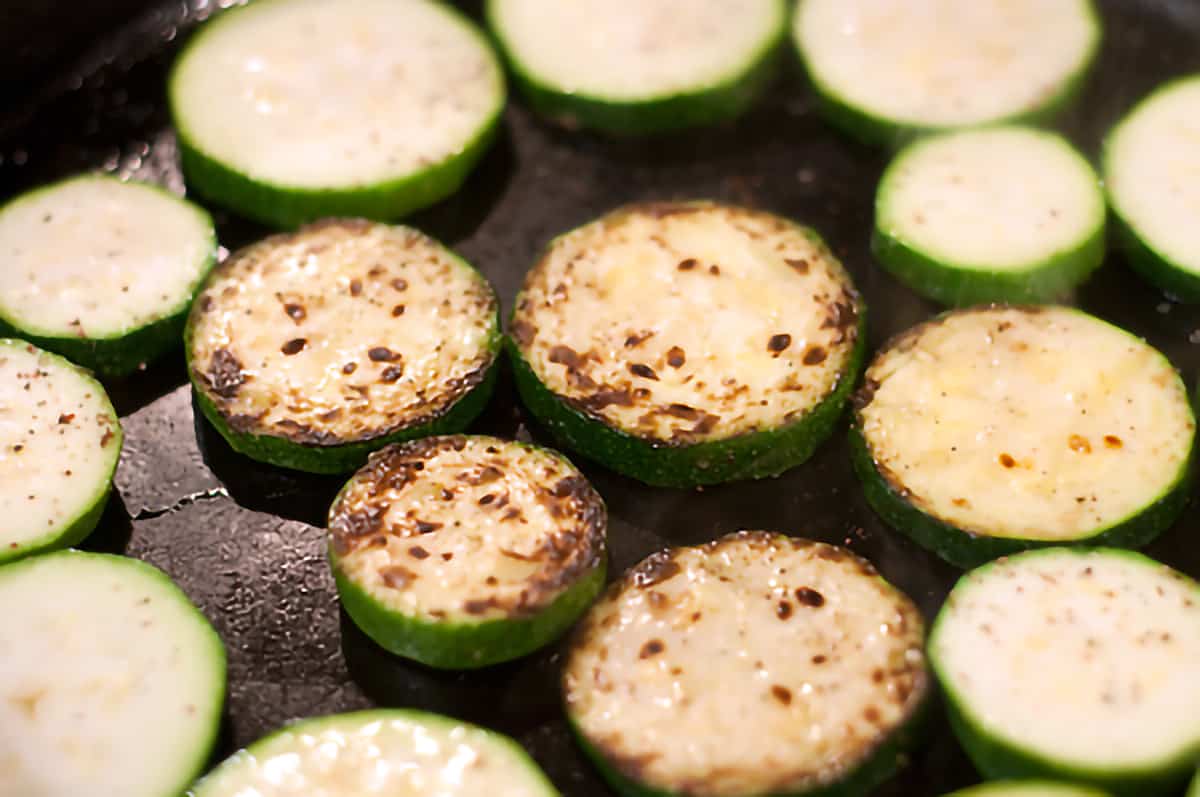 Closeup of browned zucchini slices in a heavy skillet.