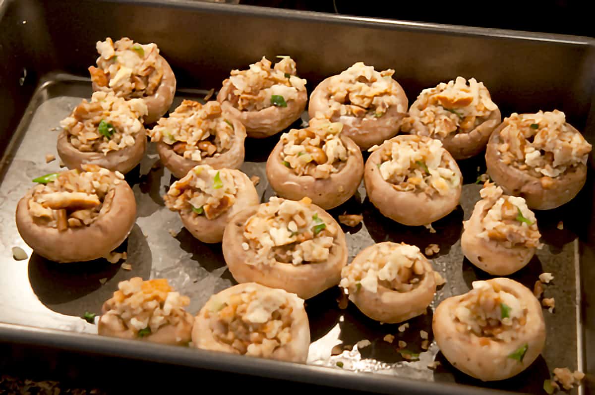 Mushroom caps filled with stuffing mixture sitting in a baking pan.
