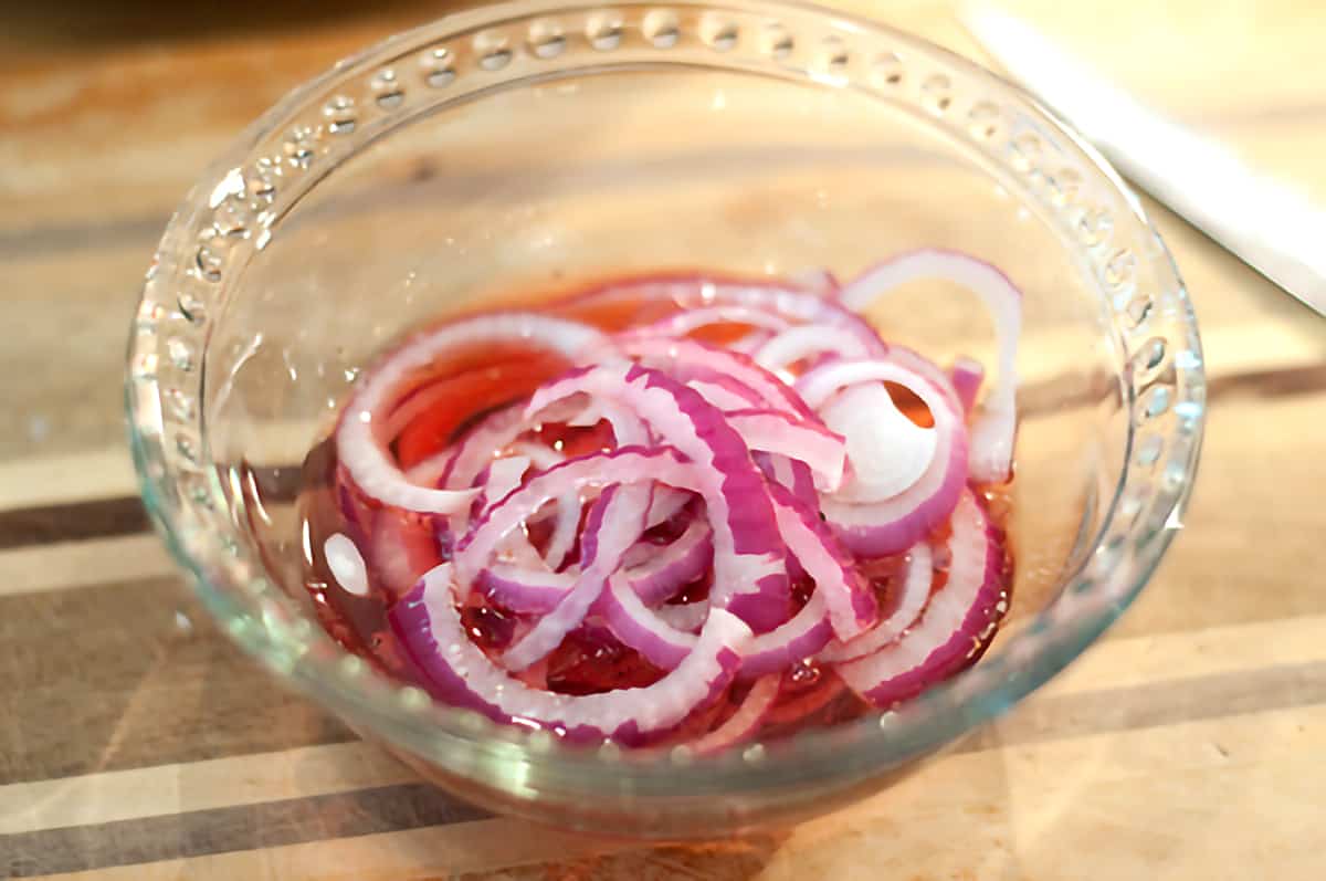 Sliced red onions in a small bowl with red wine vinegar.