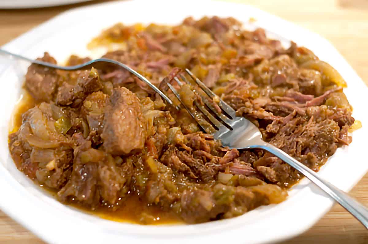 Cooked beef on a plate with two forks.