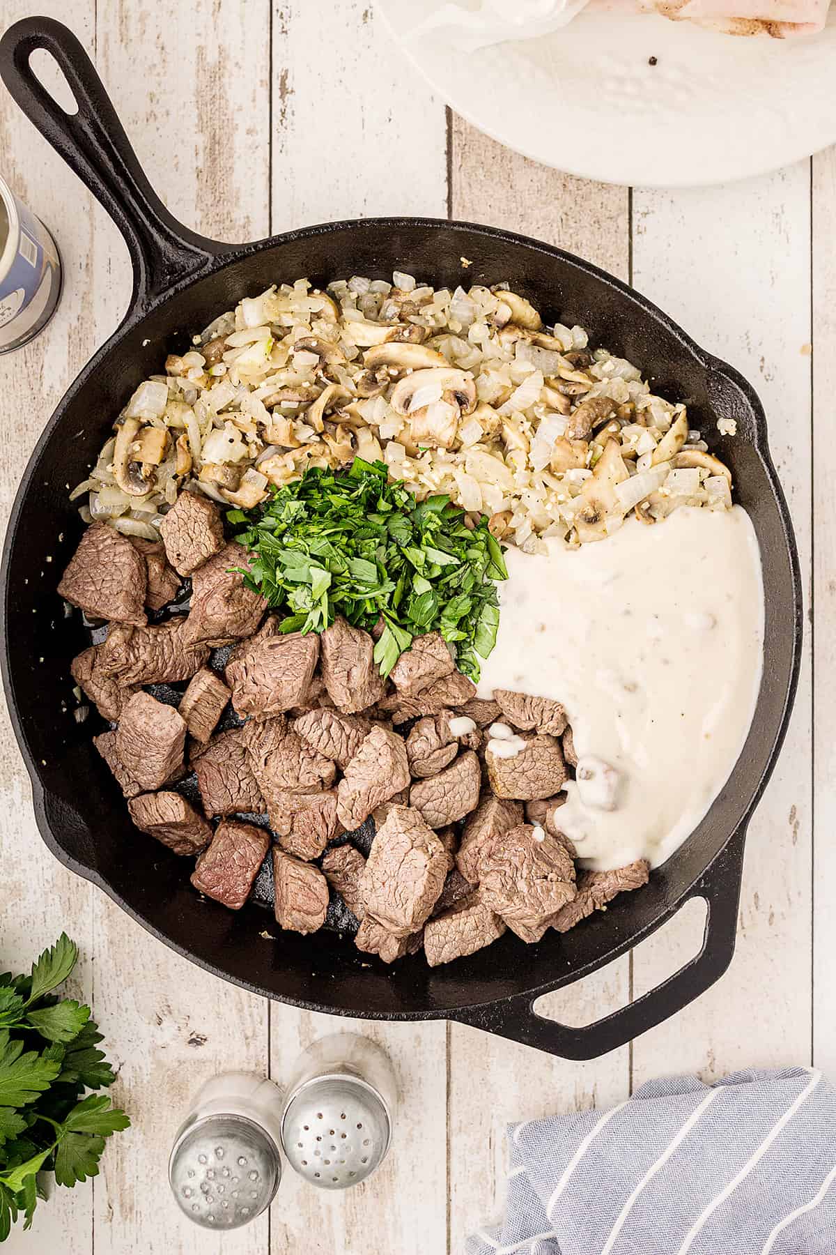 Cooked beef, vegetables, soup, and parsley added to cast iron skillet.