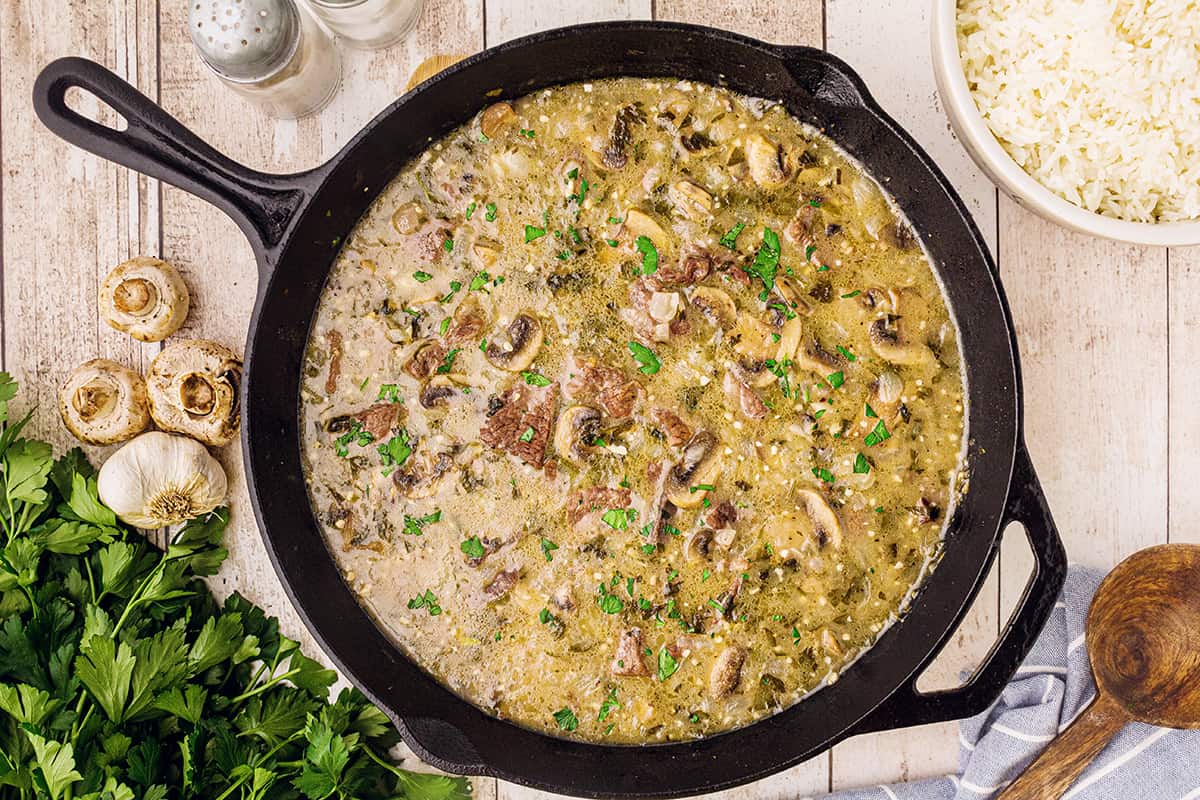 Black cast iron skillet with steak tips and creamy mushroom sauce after cooking for 1 hour.