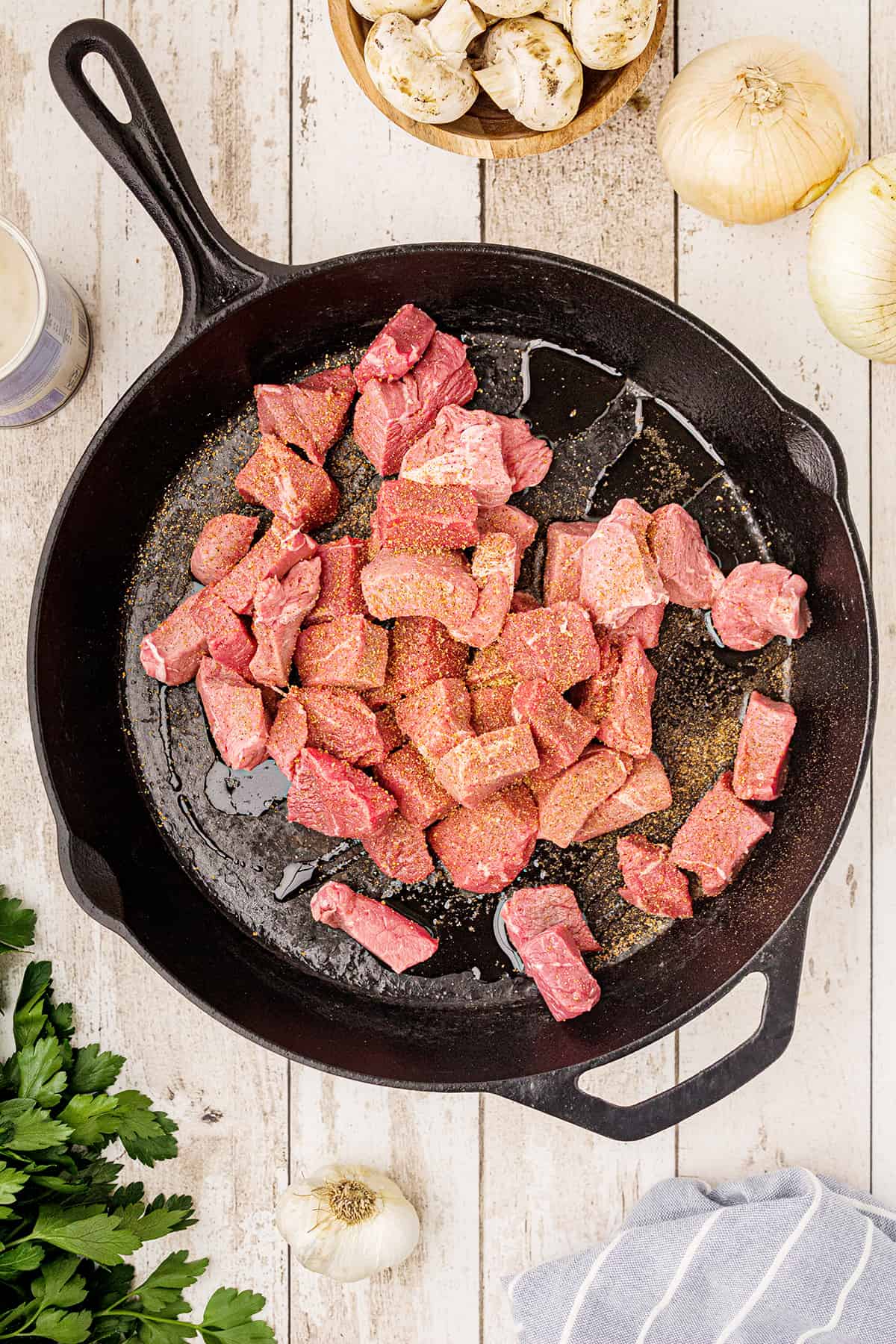 Steak tips sprinkled with seasoned salt in a cast iron pan.