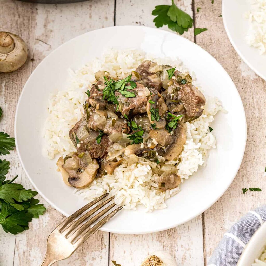 Steak tips with Creamy Mushroom Sauce over rice on a serving plate.