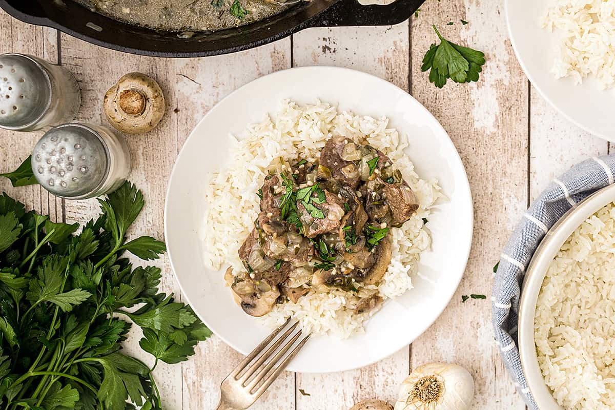 A serving of Steak Tips with Creamy Mushroom Sauce over rice on a white plate.