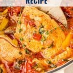 Chicken cacciatore with tomatoes, herbs, and peppers simmering in a pot with a wooden spoon.