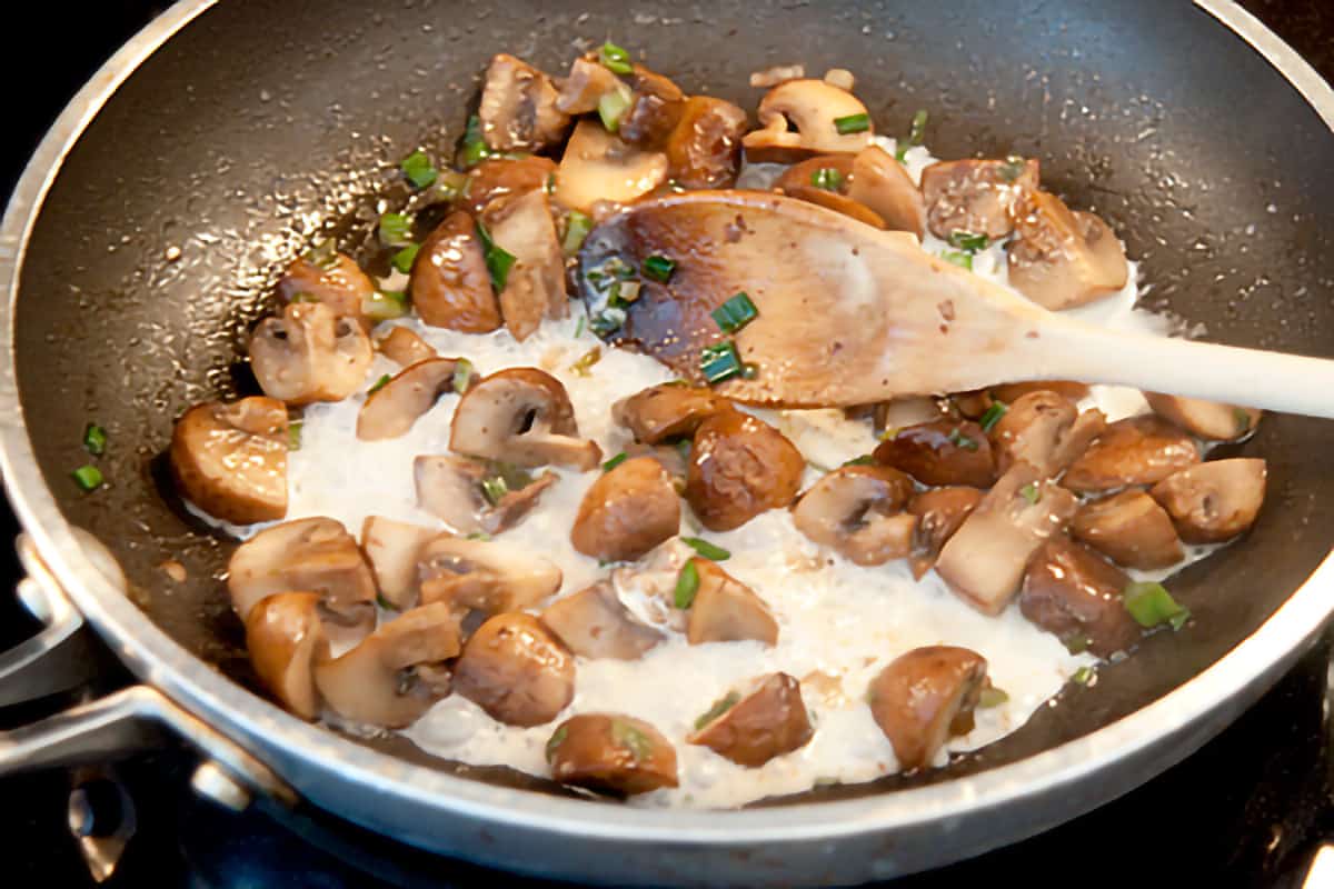 Adding cream to the cooked mushrooms and green onions.