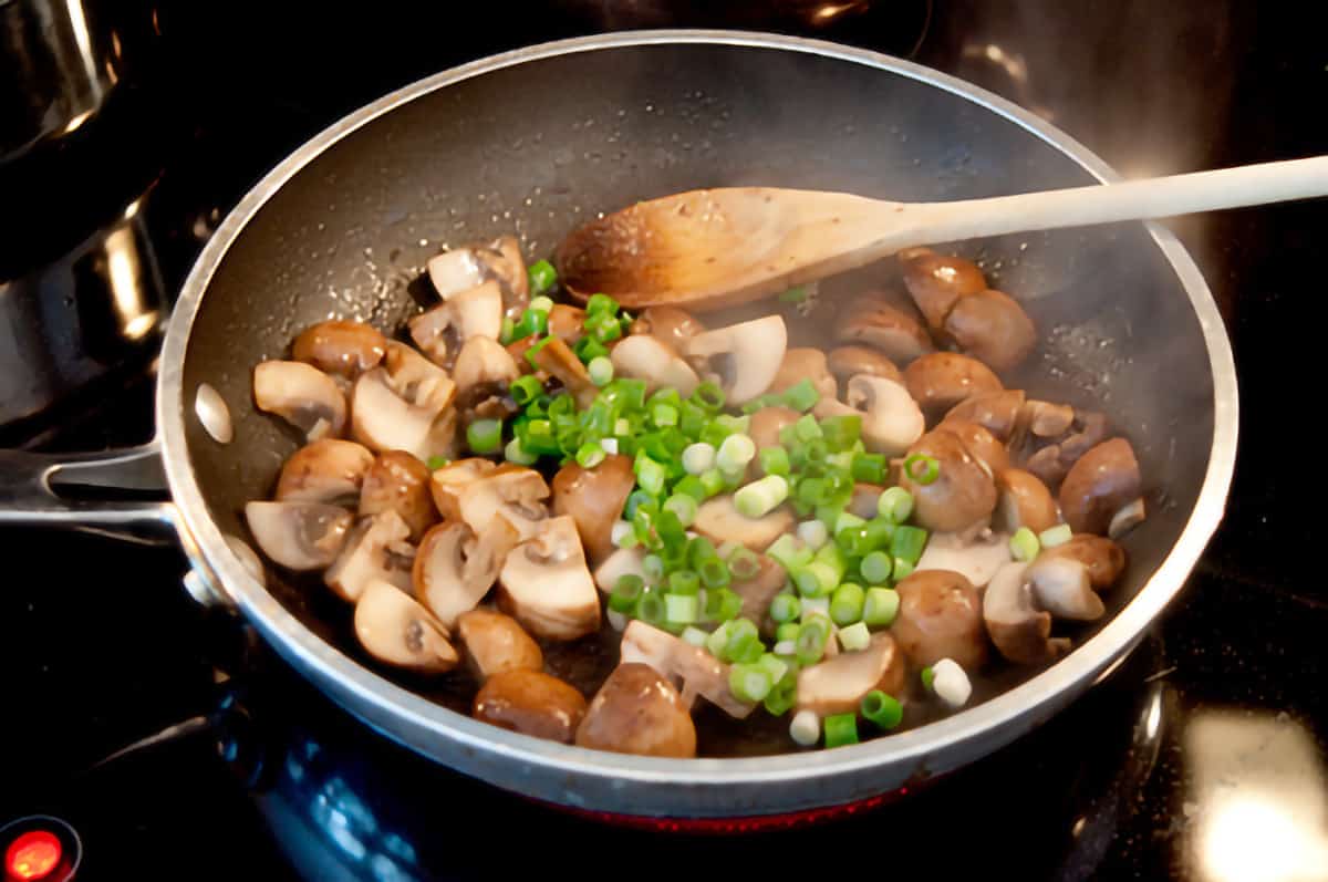 Mushrooms and green onions cooking in  a skillet.