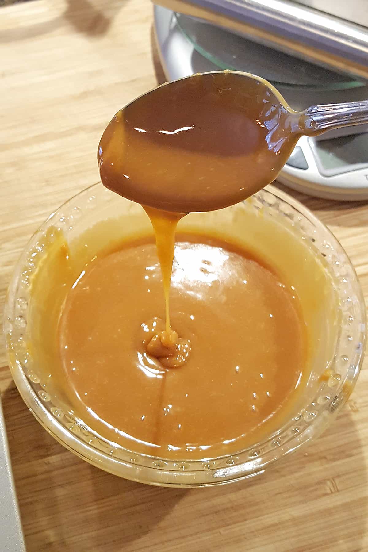 Melted caramel dripping from a spoon into a small glass bowl.