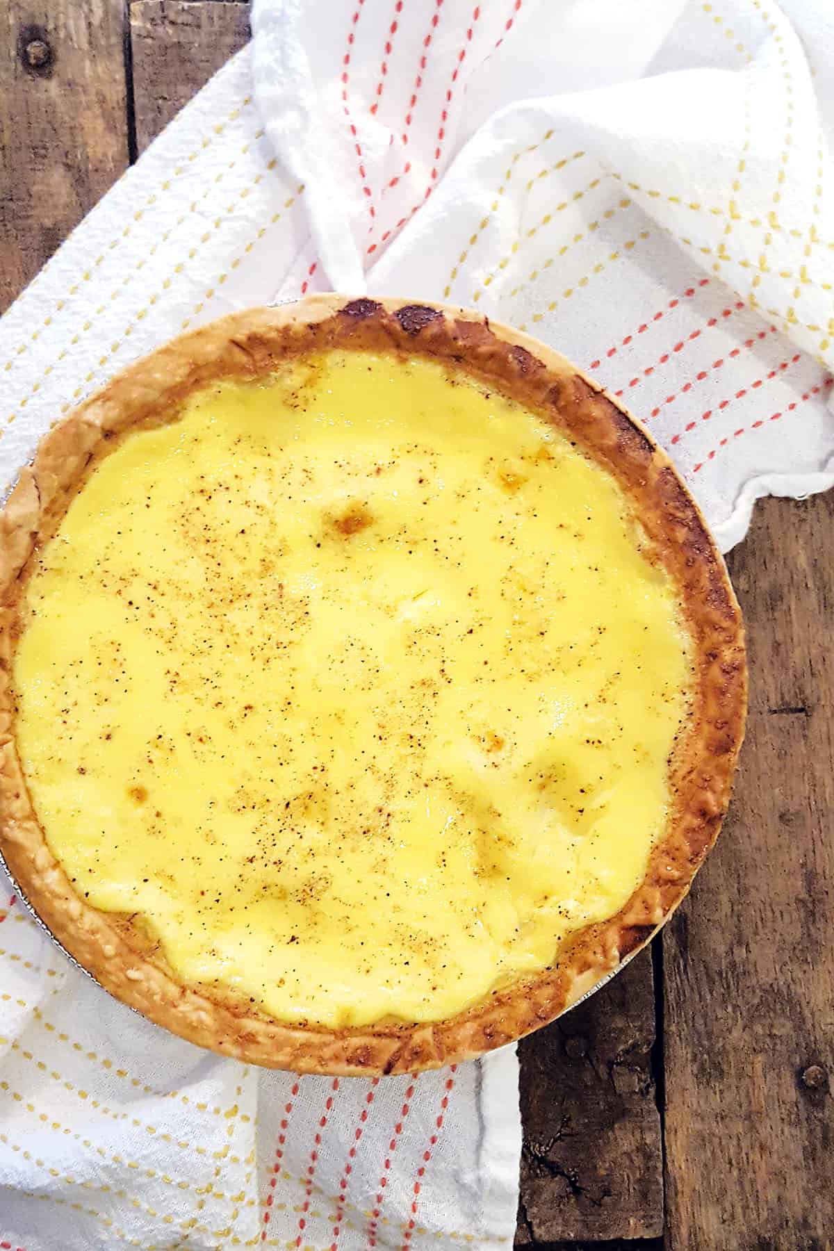 Traditional southern egg custard pie on a serving board with a kitchen towel in the background.