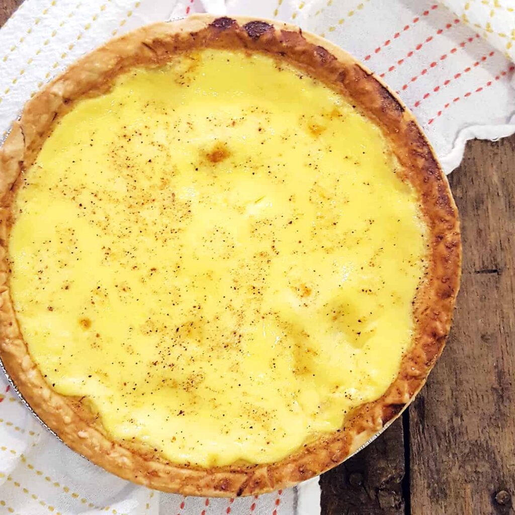 Traditional southern egg custard pie on a serving board with a kitchen towel in the background.