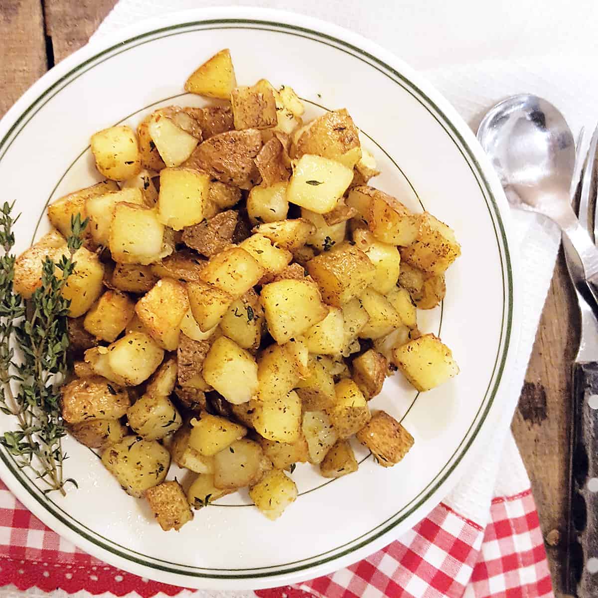 Home fries on a white plate with a kitchen towel and spoon in the background.