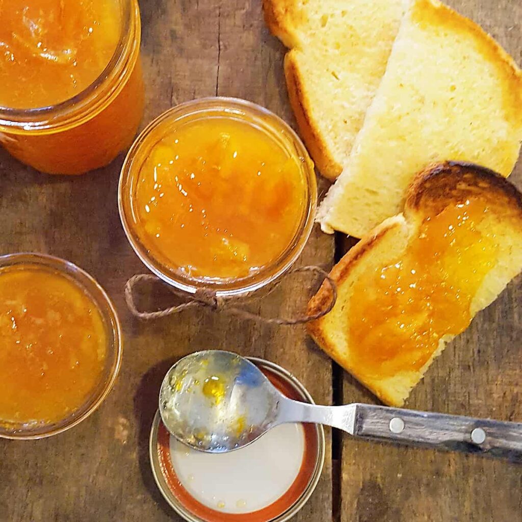 Jars of spiced orange marmalade with a spoon and toasted bread.