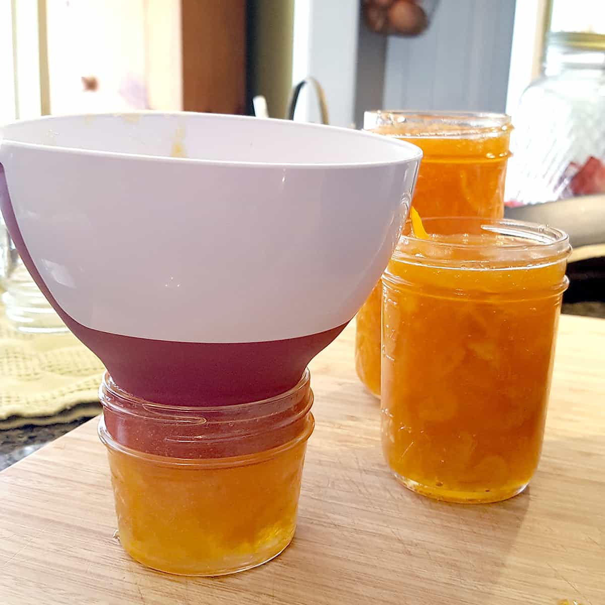 Three jars of orange marmalade and a canning funnel.