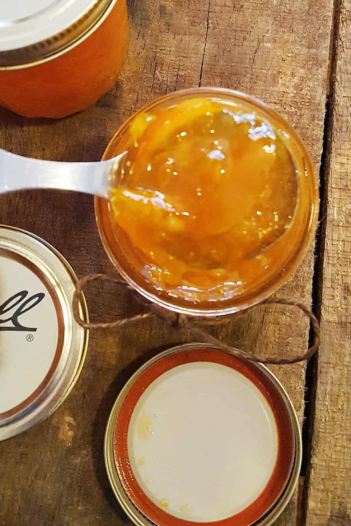 Finished Instant Pot Spiced Orange Marmalade in a spoon with jars in the background.