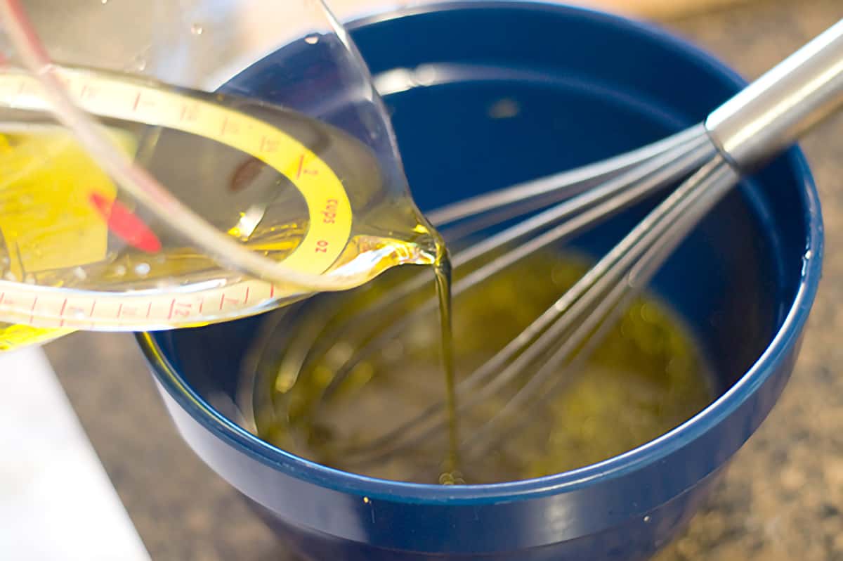 Pouring oil into a mixing bowl with dressing ingredients.