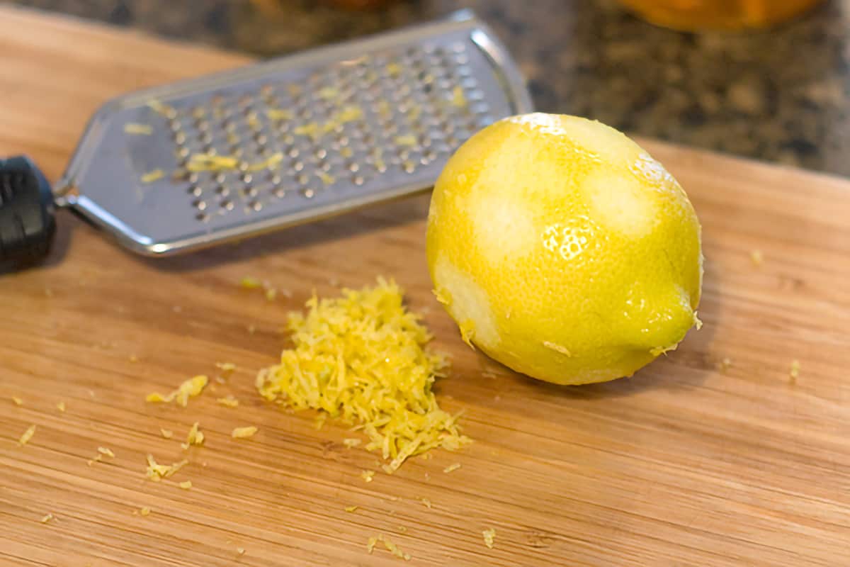 A lemon partly zested with a grated on a cutting board.