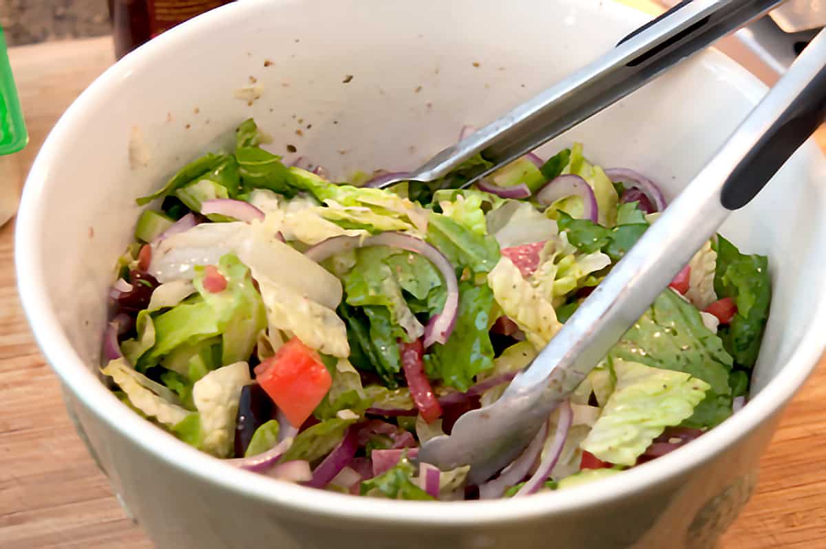 Large salad bowl containing all ingredients for the salad and a pair of cooking tongs.