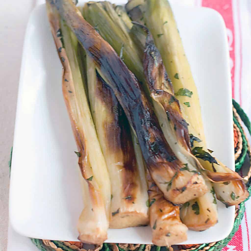 Roasted leeks on a white serving plate.