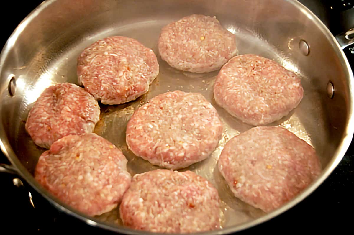 Eight sausage patties cooking in a skillet.