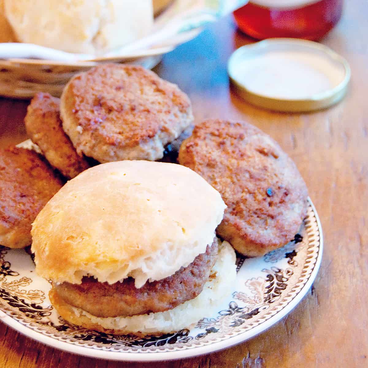 Spicy breakfast sausage patties and biscuits on a serving plate with a jar of jelly in the background.