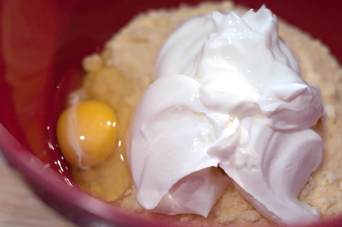 Cornbread mix, egg, and sour cream in a red mixing bowl.