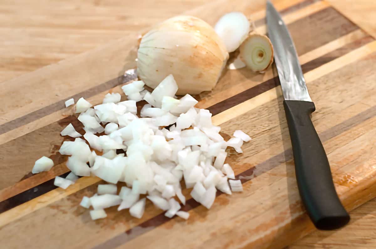 Finely chopped onion and a knife on a cutting board.