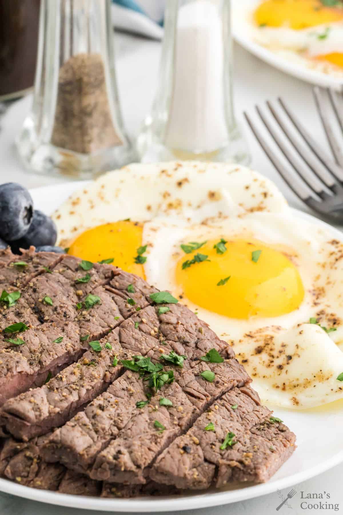 Finished steak and eggs on a white plate with salt and pepper shakers in the background.