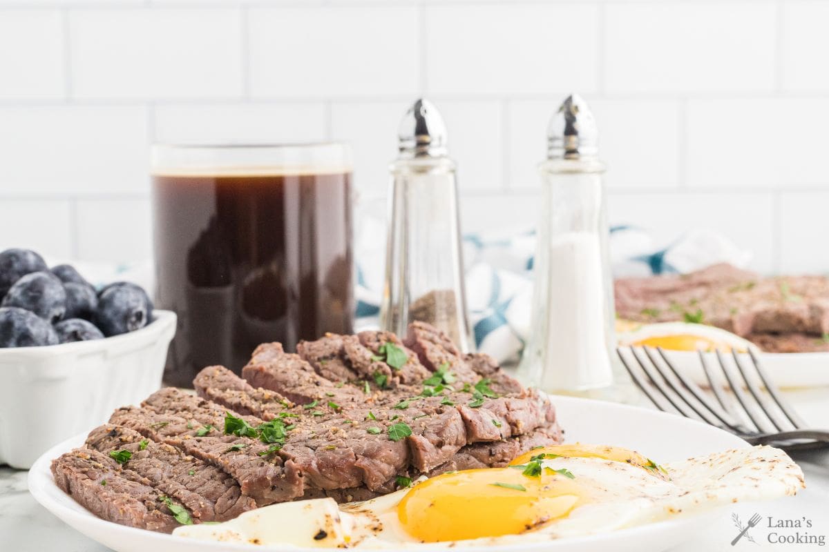 Steak and eggs with coffee and salt and pepper on a table.