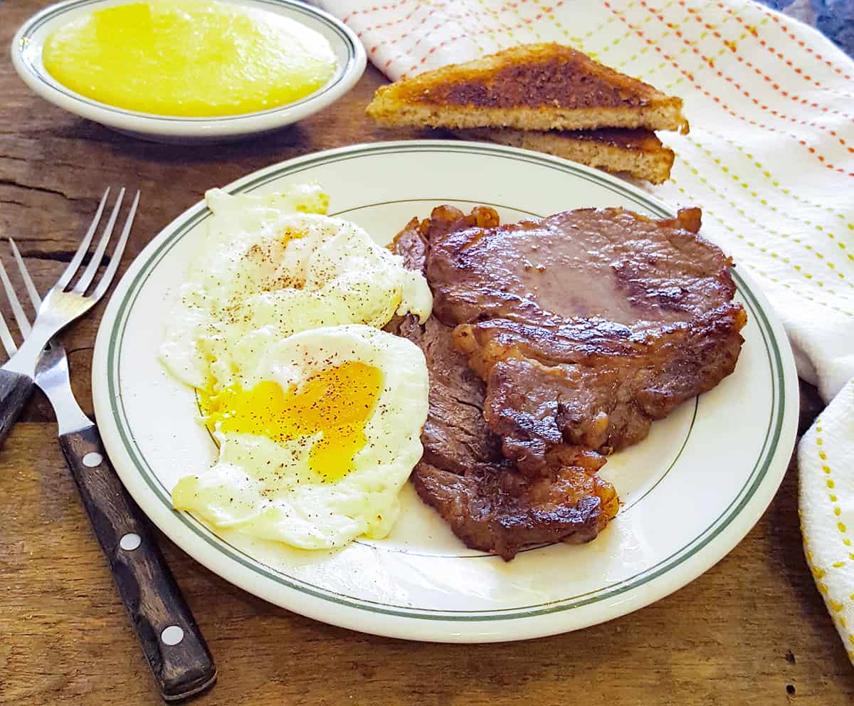 Steak and eggs on a serving plate with toast and grits alongside.