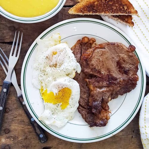 Steak and eggs on a serving plate with grits and toast on the side.