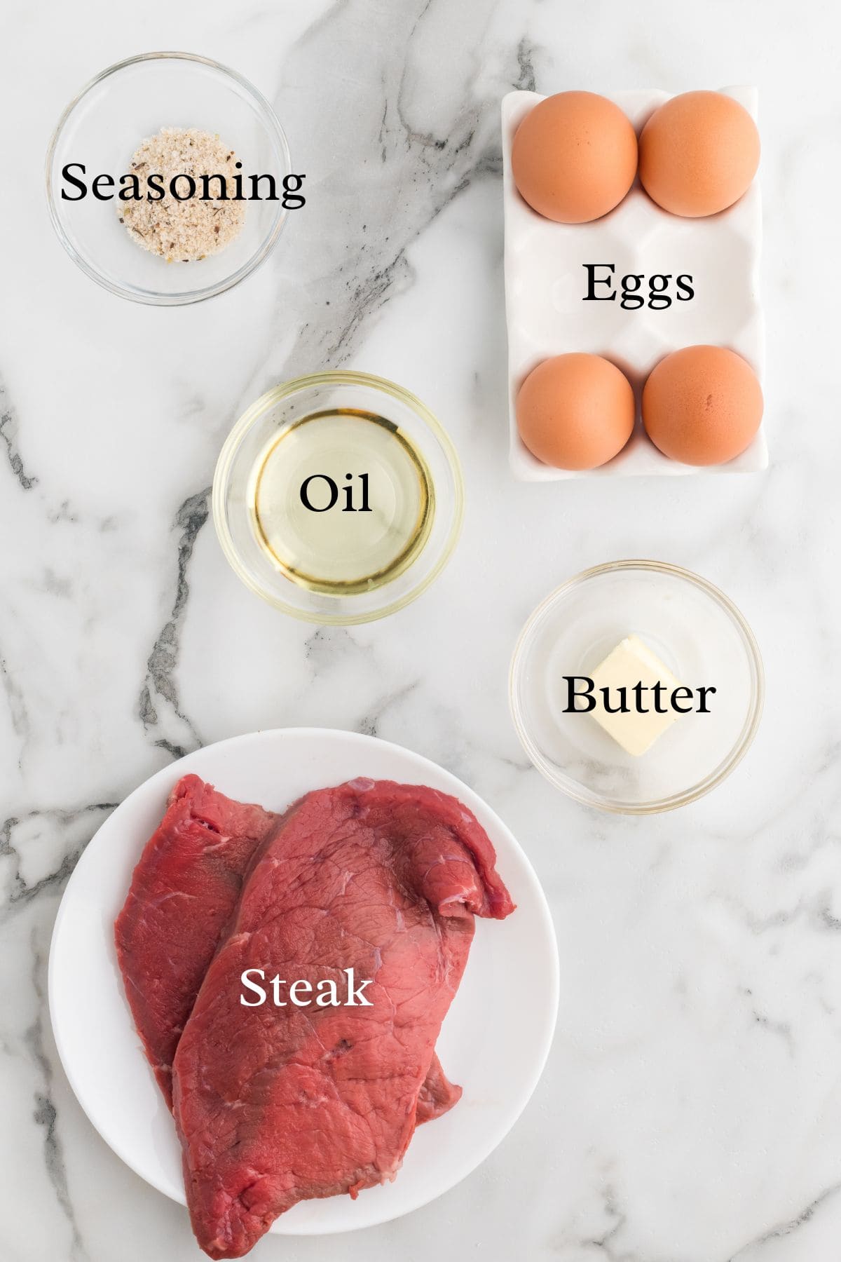 Ingredients for steak and eggs on a marble background in separate containers.