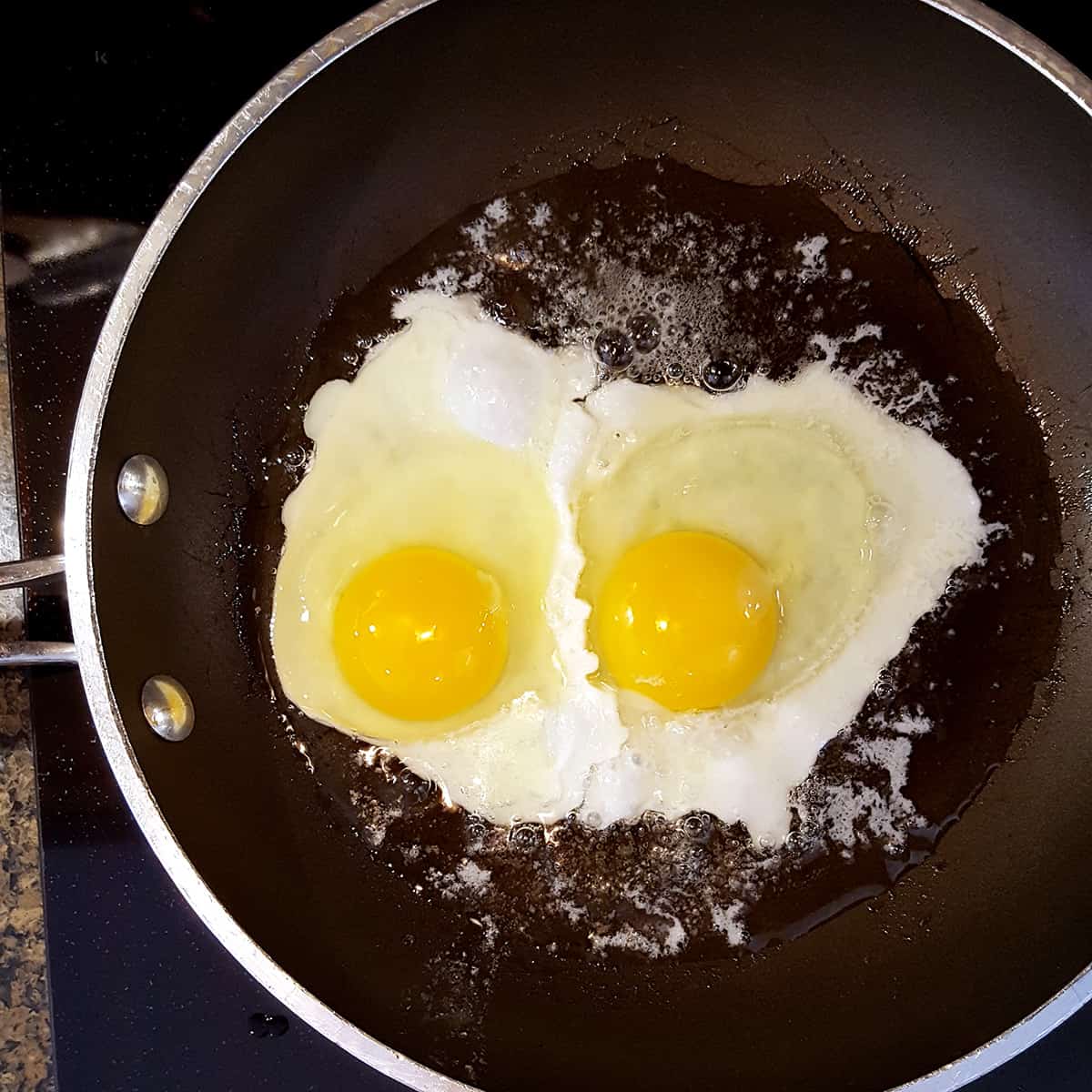 Two eggs cooking in a skillet with butter and oil.