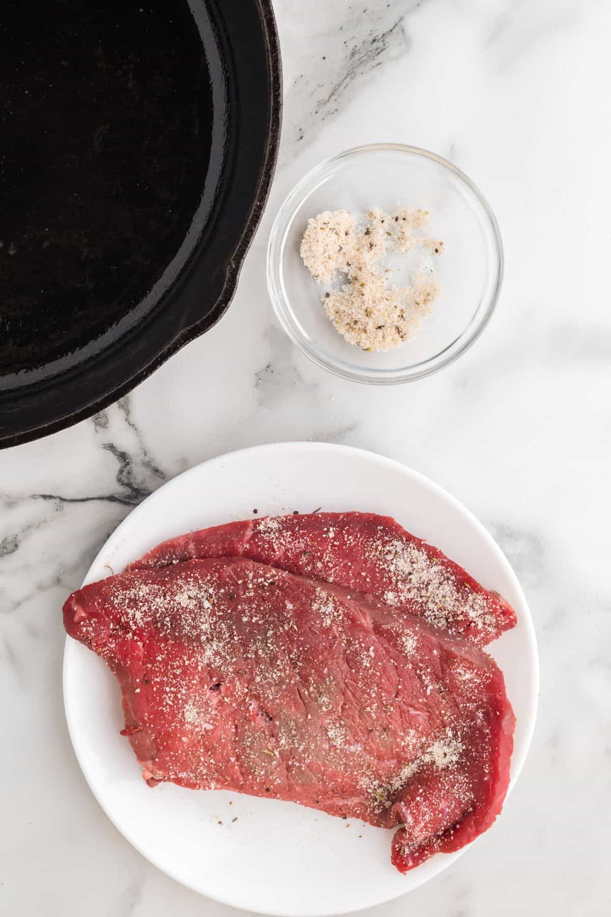Seasoned steak on a white plate on a marble background.