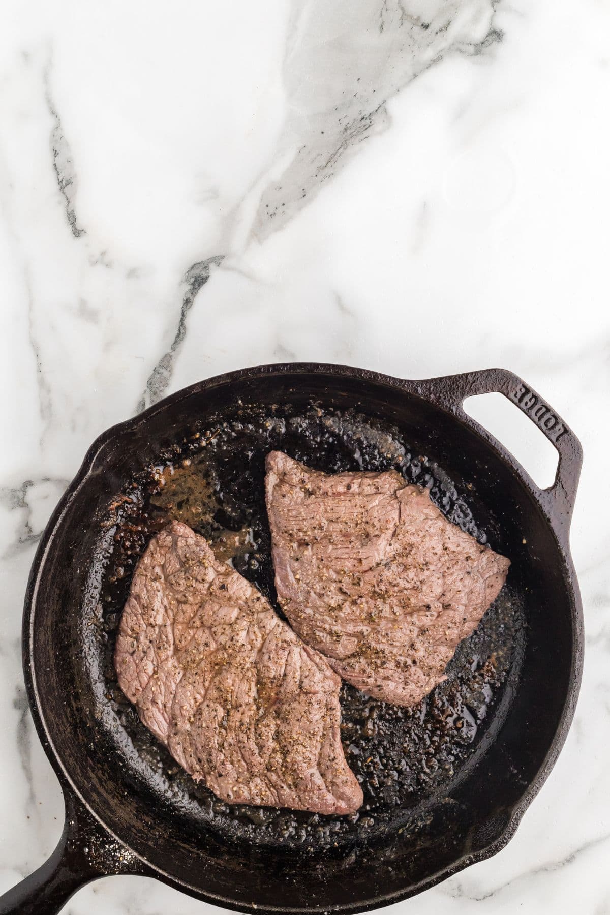 Steaks after being flipped once while being cooked in a cast iron skillet.