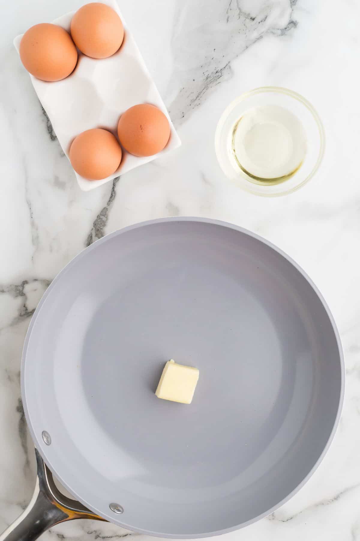 Butter in a non-stick skillet being being heated. Pictured with eggs and oil on the side.