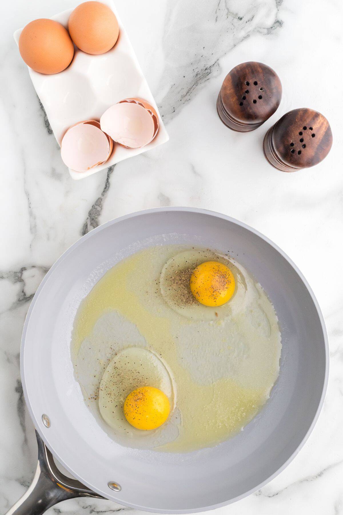 Seasoned eggs cracked into the preheated skillet on a marble background.