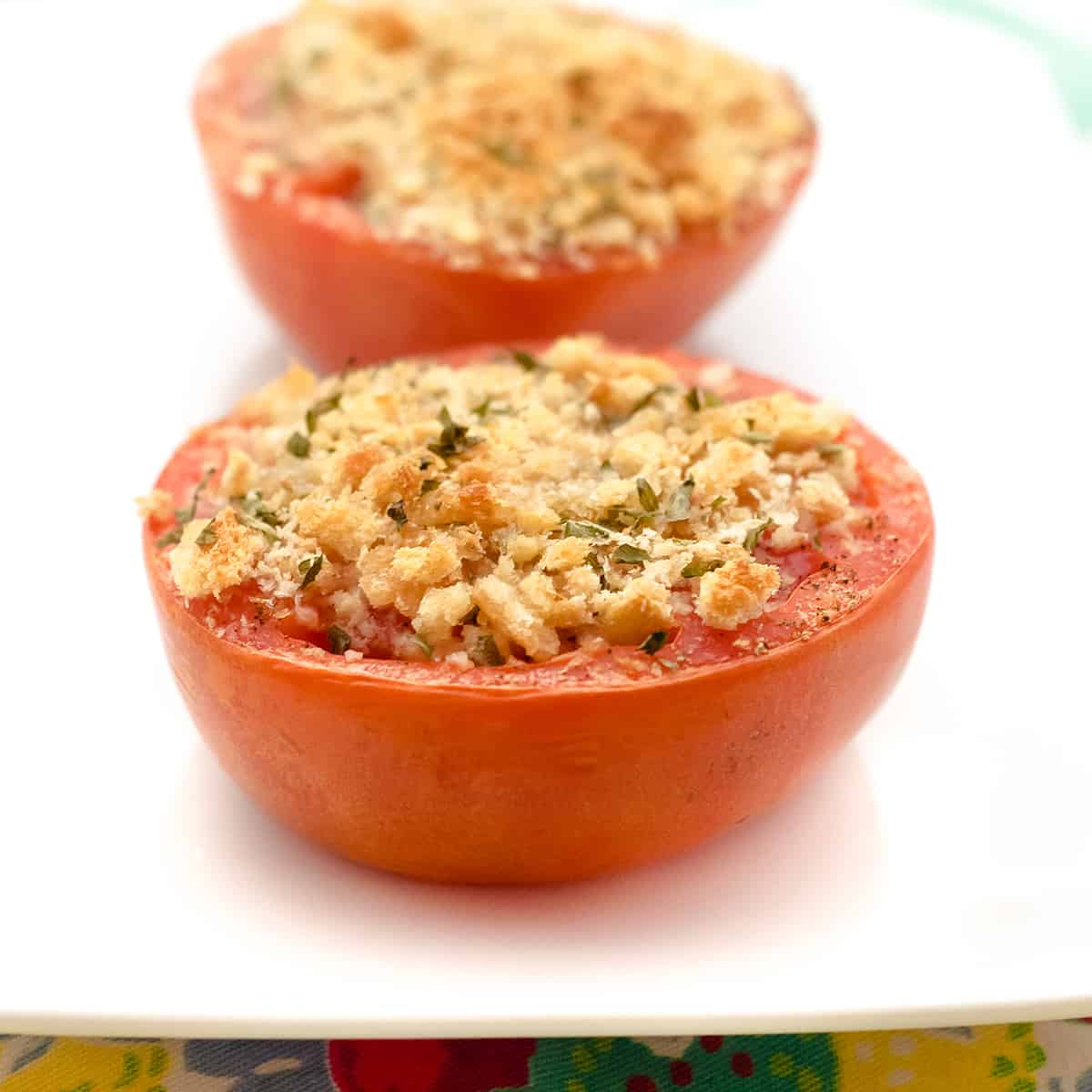 Tomatoes topped with breadcrumbs and herbs on a serving plate.