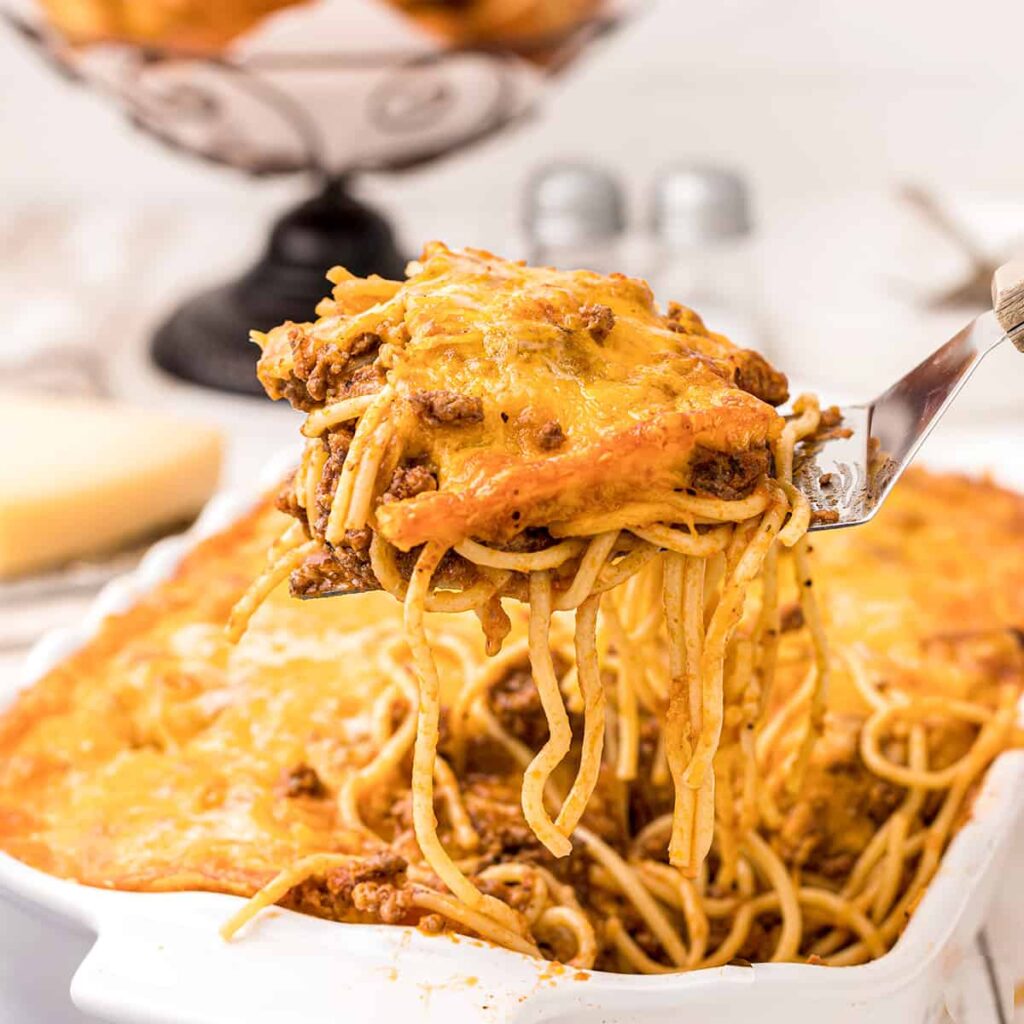 A forkful of baked spaghetti dripping with cheesy topping and meat sauce.