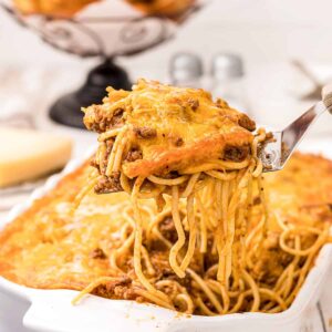 A forkful of baked spaghetti dripping with cheesy topping and meat sauce.
