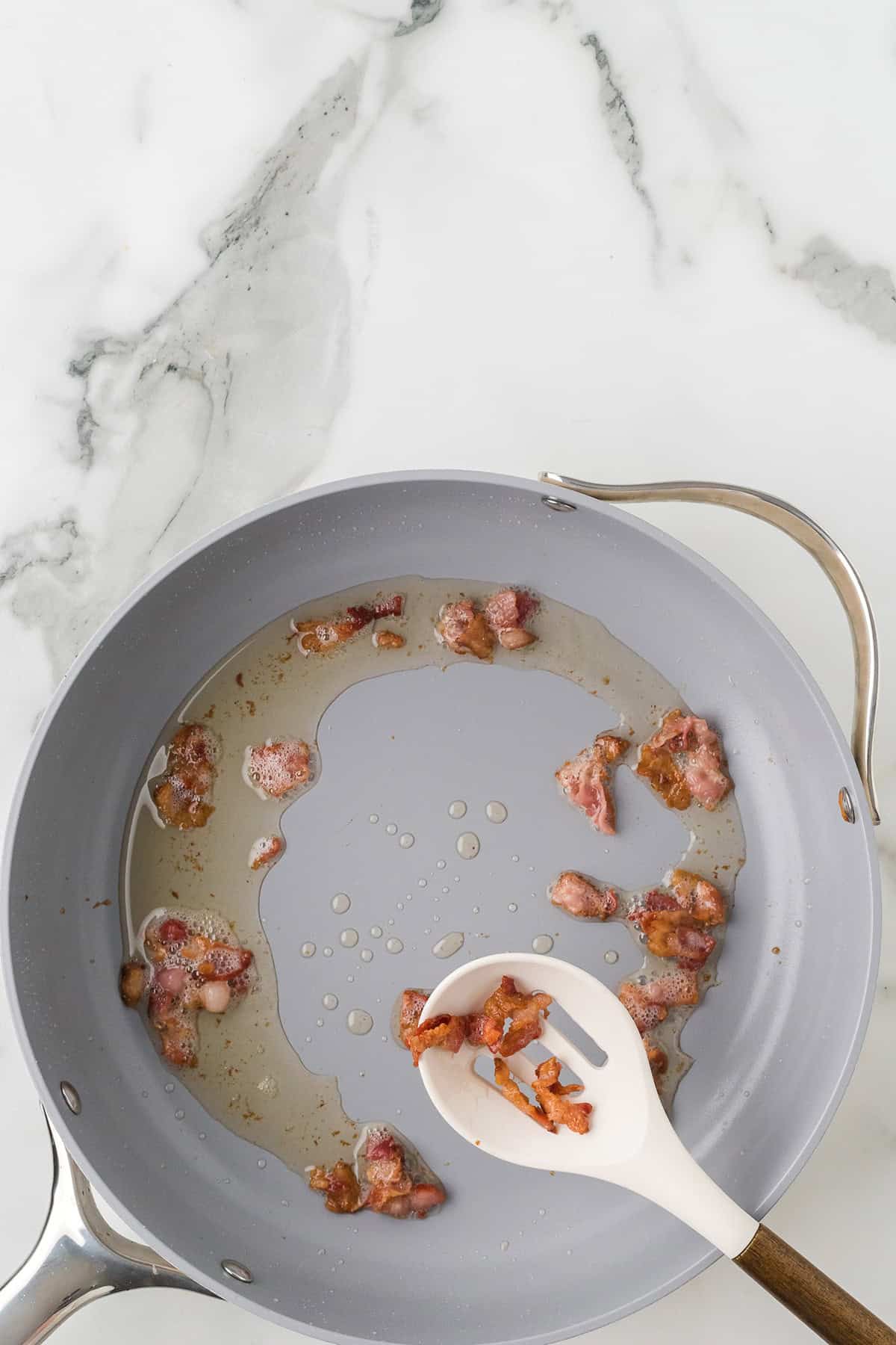 Removing the bacon from the skillet using a slotted spoon.