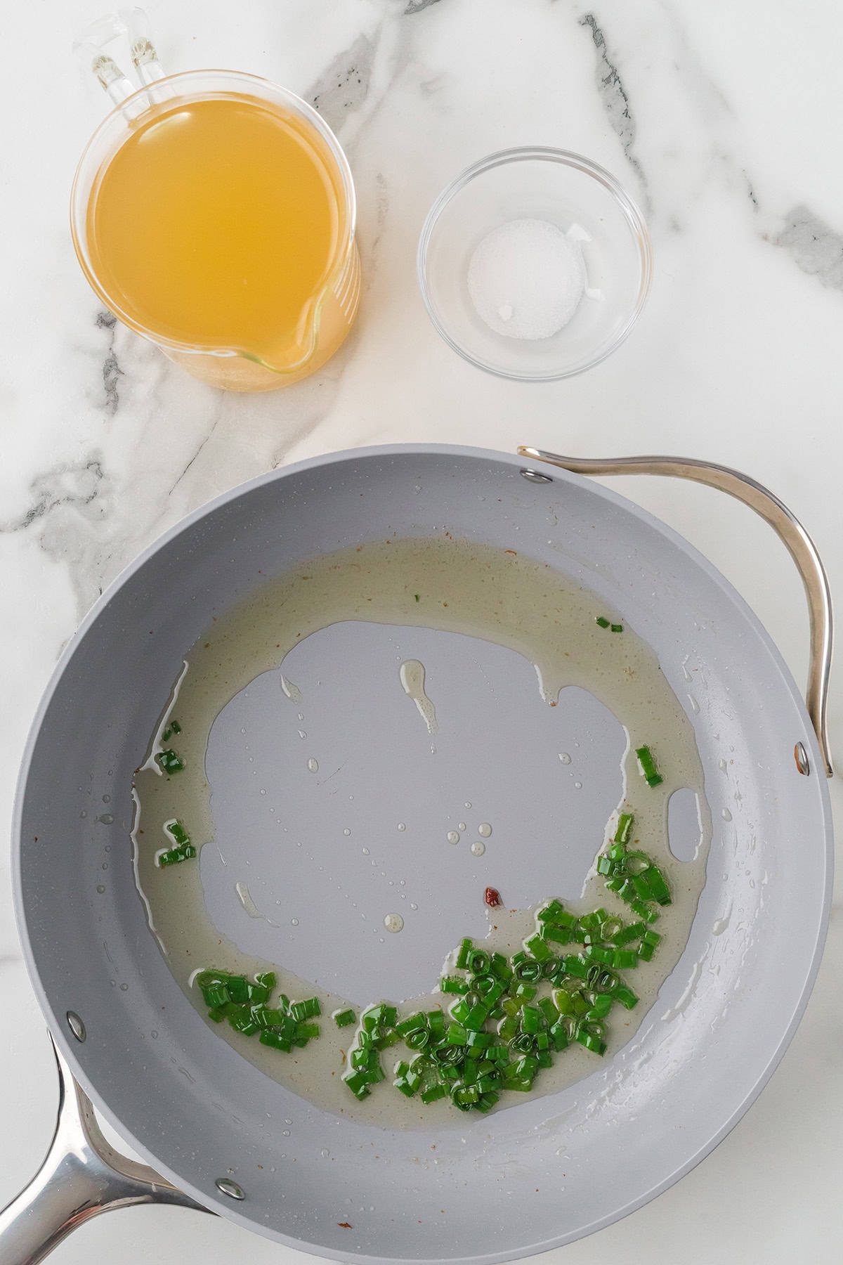 Sliced green onions added to bacon fat in a skillet.