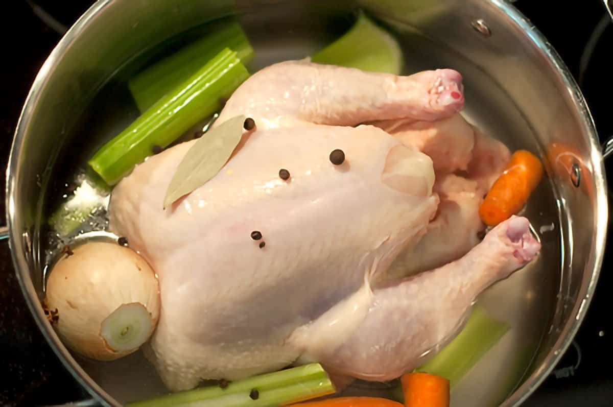 Whole chicken and aromatic vegetables in a stock pot.