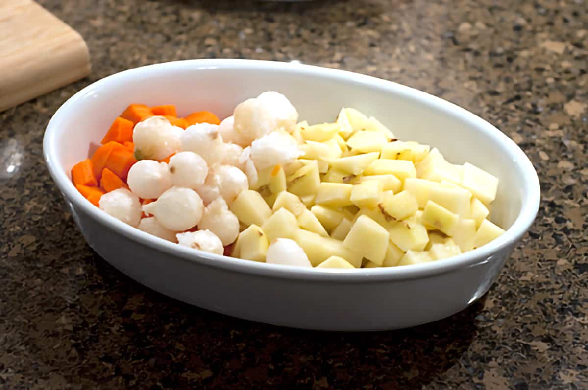 Veggies for Chicken Pot Pie Carrots, potatoes, and pearl onions in a ceramic baking dish.