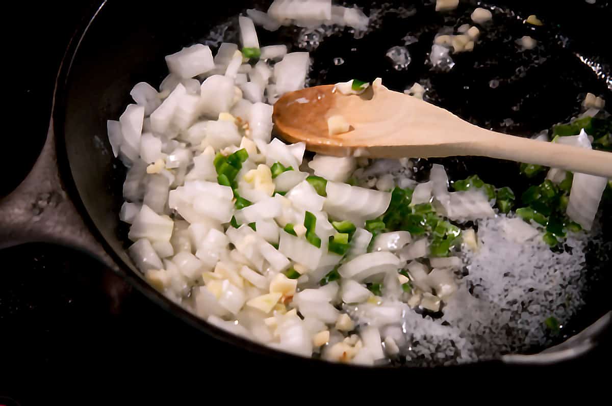 Onion, garlic, and jalapeno cooking in a cast iron skillet.